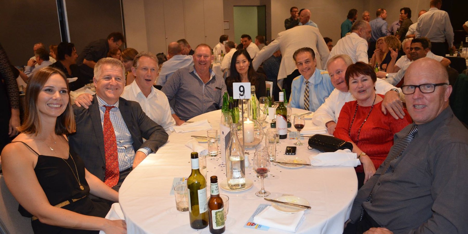 A full table of Wakehurst members and partners in jackets and ties at a club dinner, the room behind them packed with other tables.